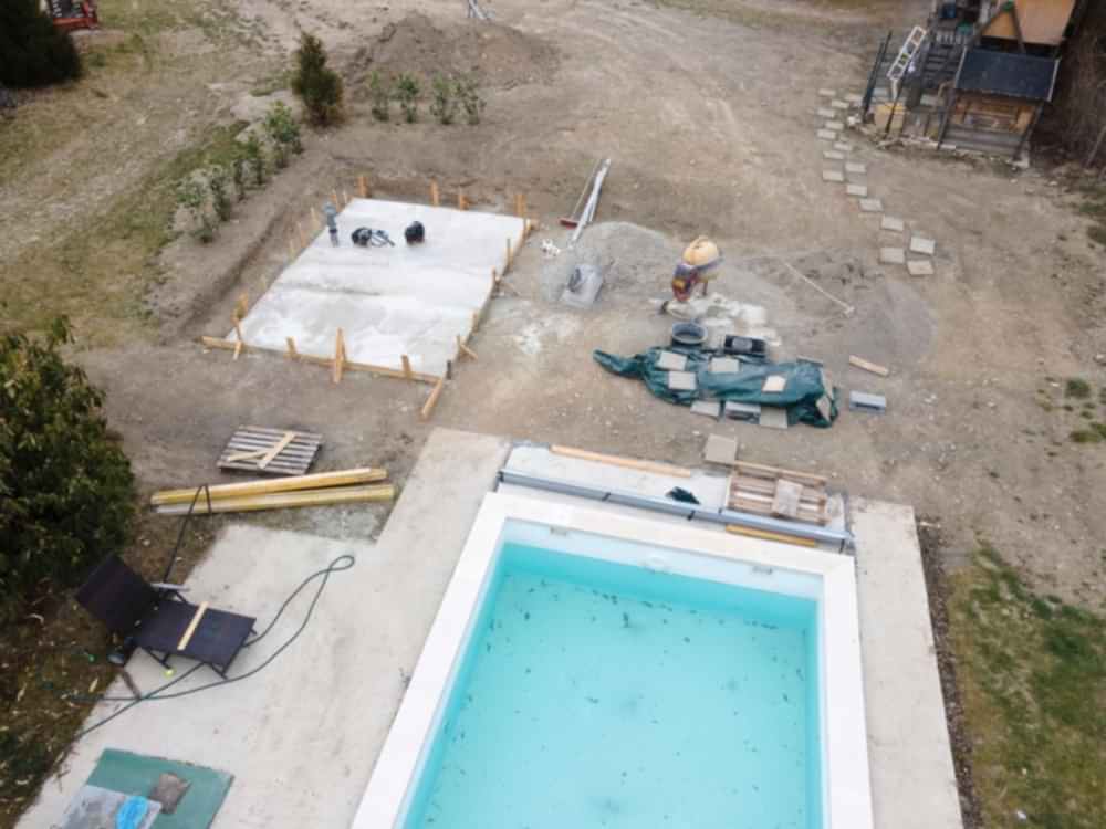 Drone shot of pool construction site with concrete pad for heat pump and pool house in garden in austria